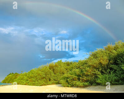 Spektakuläre Regenbogen auf weißem maledivischen Strand im Himmel mit farbigen Wolken bei Sonnenuntergang. Stockfoto