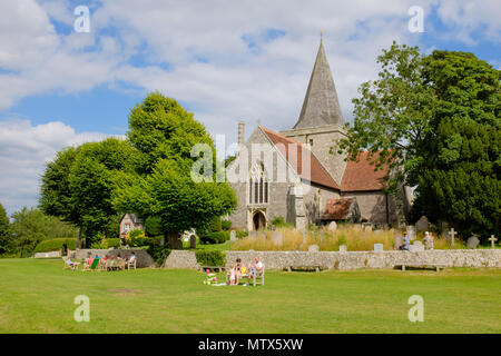 Die Kirche St. Andrew's aus dem 14. Jahrhundert befindet sich auf dem Dorfgrün in Alfriston, East Sussex, England, an einem Sommernachmittag, an dem sich die Menschen auf dem Rasen entspannen. Stockfoto