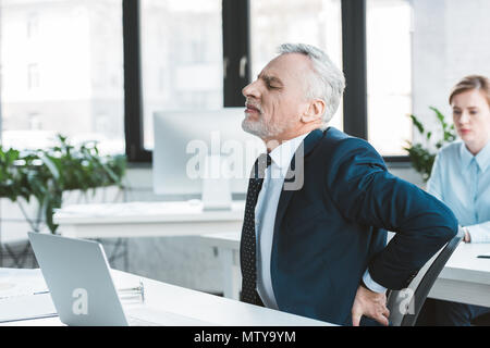 Seitenansicht der älteren Geschäftsmann leiden unter Schmerzen im Rücken beim Sitzen am Arbeitsplatz Stockfoto