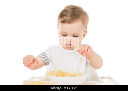 Adorable Kind essen Spaghetti mit Händen und Sitzen in Kinderhochstuhl auf weißem Hintergrund Stockfoto