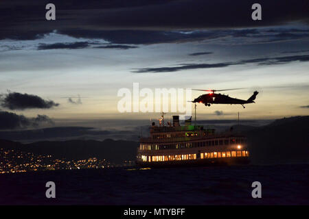 Ein fliegendes Personal an Bord eines California Air National Guard 129 Rettung Flügel HH-60G Pave Hawk Hubschrauber Positionen der Hubschrauber für Besatzungsmitglieder von der Küstenwache für die Sicherheit im Seeverkehr und Sicherheit Team 91109, in San Diego, die vor fast roping auf ein Schiff warten unten auf die Bucht von San Francisco, den 25. April 2017. Die ressortübergreifende Übung war eine Gelegenheit für die beiden Dienste zusammen, um für potenzielle Missionen Erkennen von Zug, reagiert und neutralisieren Bedrohungen offshore die Minimierung der Auswirkungen auf die Sicherheit und die Sicherheit der amerikanischen Bürger. Us-Küstenwache Stockfoto