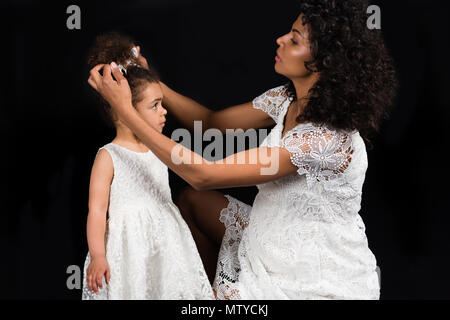 Schwangere Mutter zur Festsetzung einen Bogen zu ihrem Vorschulkind Tochter isoliert auf Schwarz Stockfoto