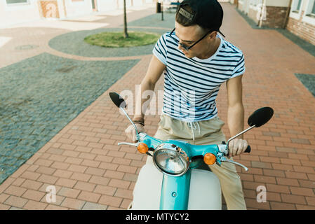 Stilvolle junger Mann in Kappe und Sonnenbrille, Moped- und nach unten schauen. Stockfoto