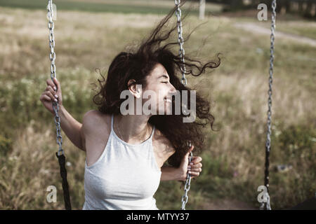 Frau mit windswept Haare auf einer Schaukel sitzend Stockfoto