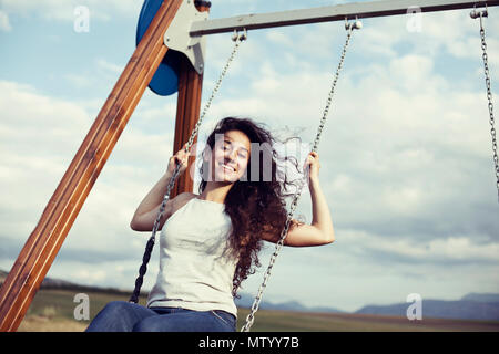 Frau mit windswept Haare auf einer Schaukel sitzend Stockfoto