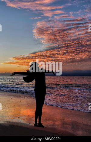 Silhouette einer Frau, die am Strand mit ihren ausgestreckten Armen Stockfoto