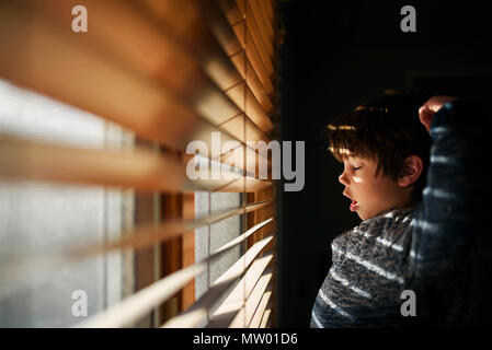 Junge durch ein Fenster Gähnen und Strecken Stockfoto