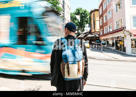 Männliche Tourist in Freizeitkleidung mit Rucksack steht vor der Straße mit Straßenbahn an sonnigen Sommertag Stockfoto