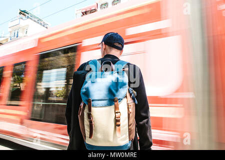 Männliche Tourist in Freizeitkleidung mit Rucksack steht vor der Straße mit Straßenbahn an sonnigen Sommertag Stockfoto