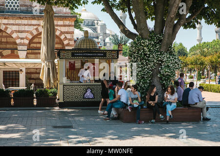 Editorial Bild einer Gruppe von Menschen, die sich auf eine Bank um schöner Baum und Anbieter arbeitet an Kamaras osmanischen Eis stand. Istanbul, Turley Stockfoto
