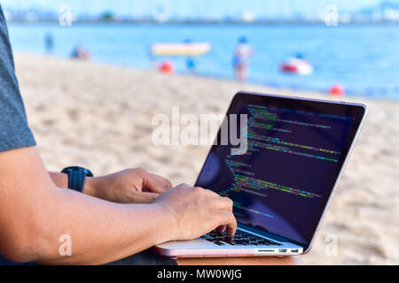 Ein Programmierer mit der Eingabe von Quellcode am Strand an einem sonnigen Sommertag. Studium, Arbeit, Technik, freiberufliche Arbeit Konzept. Stockfoto