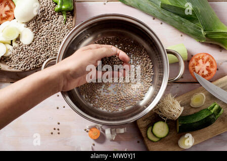 High Angle Shot eines jungen kaukasischen Mann Einführung in einen kochenden Topf Zutaten ein vegetarisches Gericht Linsen; vorzubereiten Stockfoto