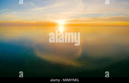 Antenne - Panoramablick auf das Meer und die untergehende Sonne über ruhigen Wasser mit Cloud Reflexionen und schönen leuchtenden Farben Stockfoto