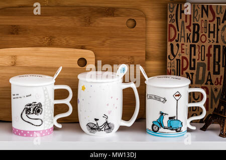 Großer weißer Becher mit Löffel und Fahrrad-, Motorrad- und Kamera Design auf weißem Regal Stockfoto