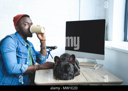 Junger Mann Kaffee trinken durch Französische Bulldogge liegen auf dem Tisch Stockfoto