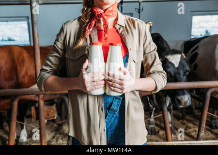 Schuss der weiblichen Bauer Holding Flaschen mit frischer Milch beim Stehen in der Nähe von Kühen im Stall 7/8 Stockfoto