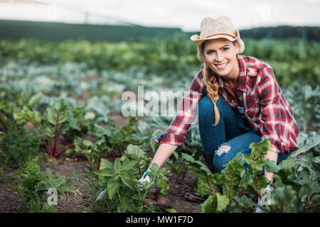 Junge weibliche Landwirt in hat die Ernte roter Bete und lächelnd an der Kamera im Feld Stockfoto