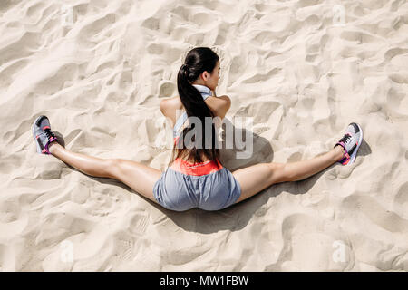 Asiatische Sportlerin mit Kopfhörern tun Split auf Sand Stockfoto