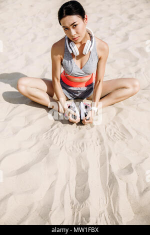 Brunette asiatischen Sportlerin mit Kopfhörern stretching auf Sand Stockfoto