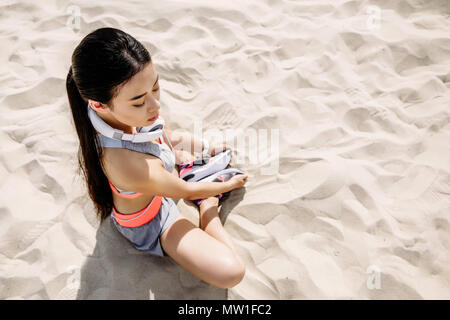 Attraktiven asiatischen Sportlerin mit Kopfhörern stretching auf Sand Stockfoto