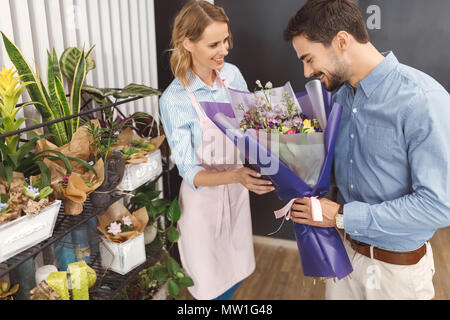 Lächelnd weibliche Blumenhändler auf bärtige junge Client duftende Blumen in Flower Shop Stockfoto