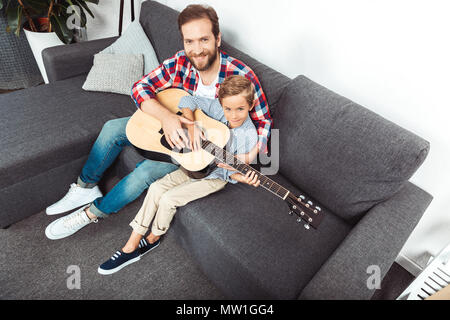 Hohe Betrachtungswinkel und der Vater mit dem Sohn Gitarre spielen und lächelnd an Kamera Stockfoto