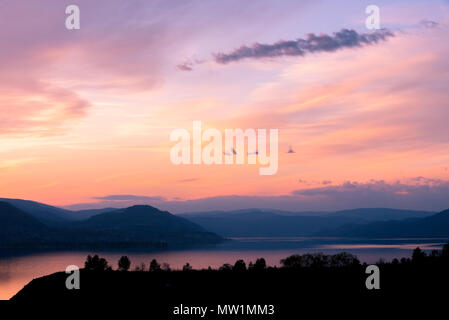 Am abend sonnenuntergang himmel über See mit sihouettes der Berge und Bäume Stockfoto
