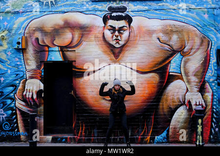 Eine Frau steht vor dem riesigen japanischen Schwergewicht Sumo Wrestler Graffiti in Brick Lane, London, Großbritannien. Stockfoto