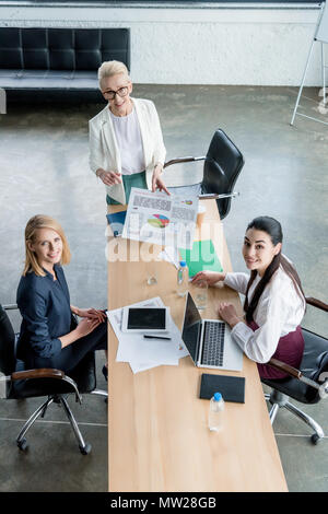 Hohe Betrachtungswinkel von Unternehmerinnen Lächeln auf die Kamera, während zusammen in die Arbeit im Büro Stockfoto