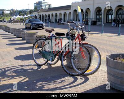 Fahrräder auf der Straße geparkt Queen Elizabeth Dr am Bondi Beach in Sydney, Australien. Fahrenden Autos, Menschen und der Vorderseite der Bondi Pavillon. Stockfoto