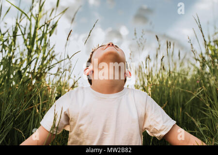 Junge in einem Feld von hohem Gras sitzen bis in den Himmel schauend Stockfoto