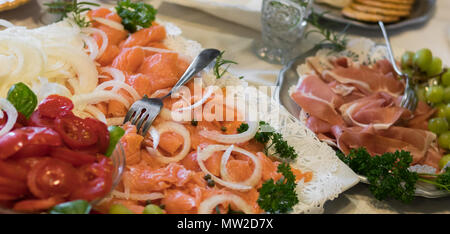 Gourmet Teller mit geräuchertem Lachs, Tomaten, Zwiebeln, Bremssättel, Prosciutto, und Trauben. Stockfoto