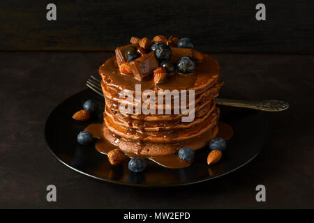 Stapel von Schokolade Pfannkuchen mit Puderzucker, Blaubeere, Mandel, Haselnuss und Schokolade. Selektive konzentrieren. Stockfoto