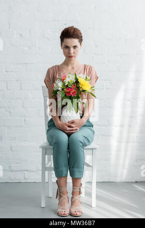 Schöne junge Frau mit Blumen in Vase vor der weißen Wand Stockfoto