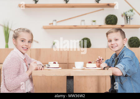 Kinder sitzen am Tisch im Cafe, während bei anderen Kamera schauen und lächeln Stockfoto