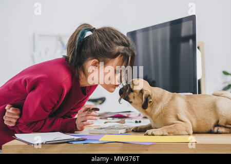 Hübsche Dame küssen pug während der Arbeit auf Illustrationen im Home Office Stockfoto