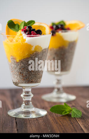 Chia Pudding mit Mango, Obst und Beeren dekoriert mit Minze auf einem Holzbrett vor einem weißen Hintergrund Stockfoto