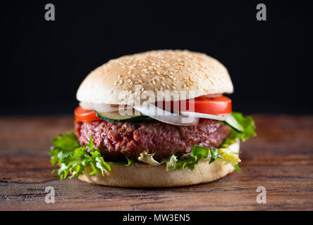 Hamburger auf dunklem Holz mit dunklem Hintergrund. Medium mit Salat, Zwiebel und Tomate. Stockfoto