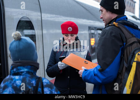 Sankt Petersburg, Russland: ein Zugbegleiter in einem roten Barett eines Sapsan Express Zug Kontrollen in einem Passagier mit einem Kind mit elektronischen Gerät. Stockfoto