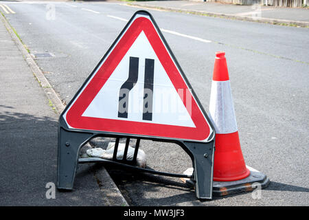 Schild in Großbritannien. Straße verengt von Links, und ein Straße Kegel Stockfoto