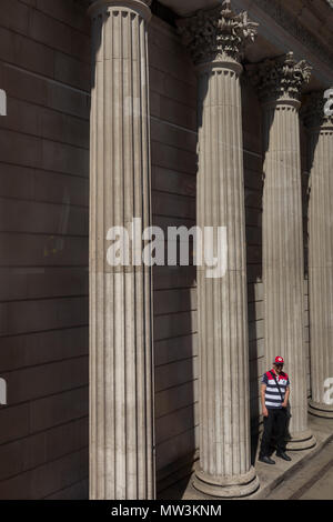 Ein Mann wartet auf einen Bus unter der Pfeiler und Säulen der Bank von England auf Threadneedle Street in der City von London, Financial District aka der Hauptstadt der Square Mile, die am 15. Mai 2018 in London, Großbritannien. Stockfoto