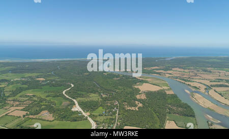 Fluss durch Ackerland und fließt in das Meer. Philippinen, Luzon. Luftaufnahme von Fluss, landwirtschaftliche Flächen gegen den blauen Himmel. Stockfoto