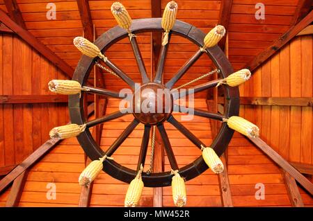 Braun woody Wagen Rad an der Decke dekoriert mit Maiskolben Stockfoto