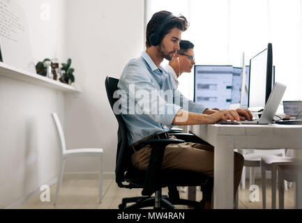Software Entwickler im Büro sitzen, arbeiten am Computer, Kopfhörer tragen. Entwickler, die an einem Notebook arbeitet im Büro. Stockfoto