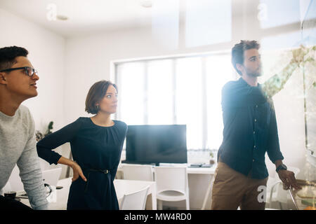 Mann schreiben an Bord im Konferenzraum, während seine Kollegen auf. Anwendungsentwickler im Diskutieren von Ideen und Arbeiten. Stockfoto