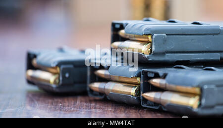 Blau Zeitschriften mit Kugeln der Feuerwaffe geputtet auf Holztisch. Munition für Schutz der Soldaten. Nahaufnahme, unscharfer Hintergrund. Stockfoto