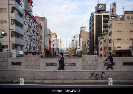 Osaka, Japan - 27. Mai 2018: ein Mann im Anzug zu Fuß auf einer Brücke über den Kanal von dotonburi einem lässig gekleideter Mann an einem Sonntag Abend Stockfoto