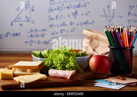 Zurück zu Schule Konzept, Schulmaterial, Auswahl an Gebäck, Papier Papier mit Nahrungsmitteln und transparente Brotdose voller Sandwich, Obst und Gemüse Stockfoto