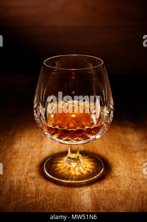 Ein Spotlight auf einem einzigen Kristall Glas Scotch Brandy, Schuß auf einen hölzernen Tisch. Stockfoto