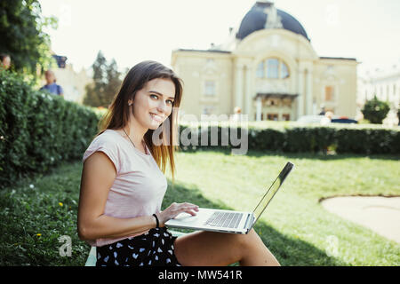 Junge Frau mit Laptop sitzen auf Gras in der Stadt. Stockfoto